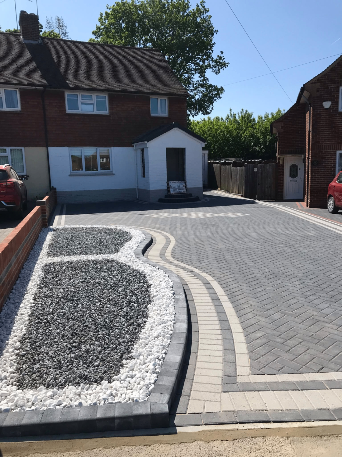 Block paved driveway with charcoal blocks and red border in front of a brick home